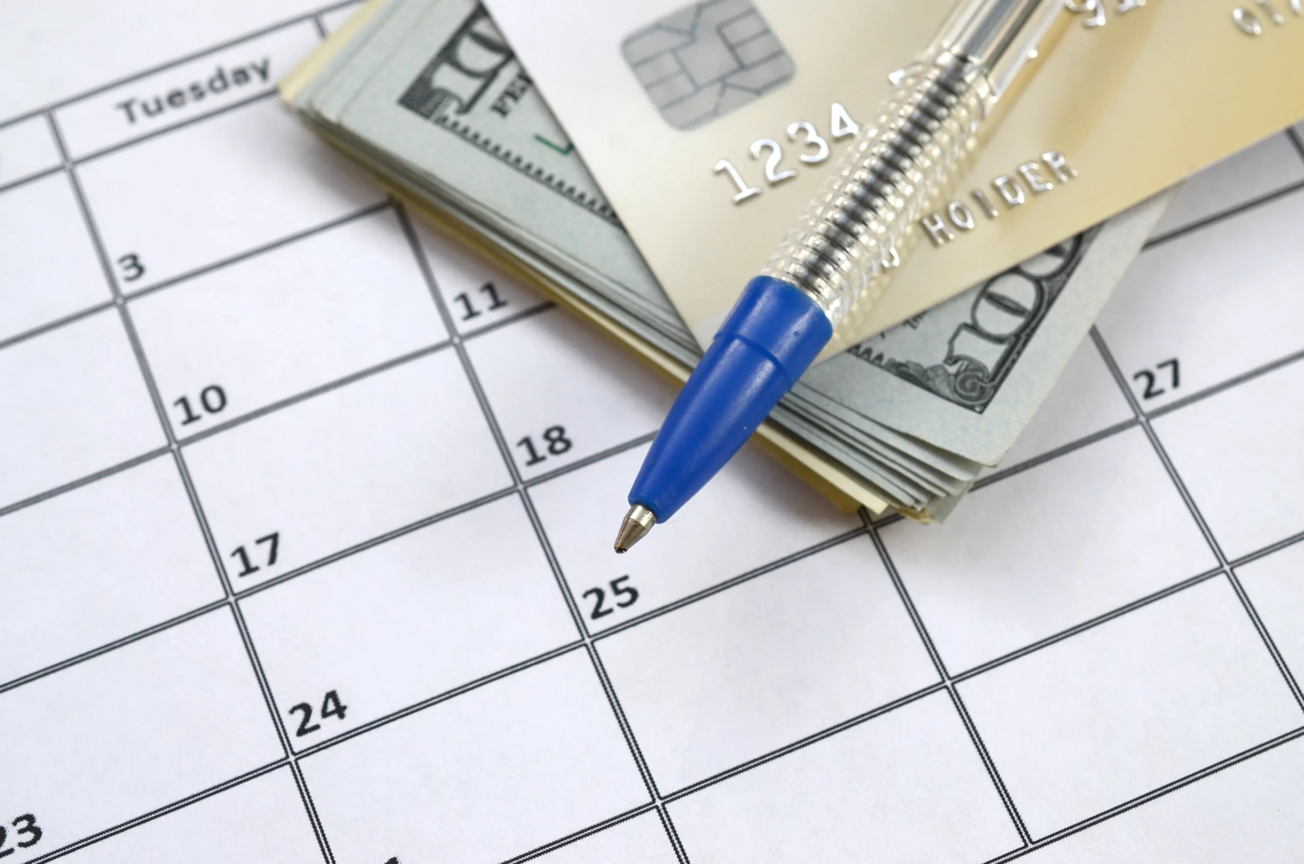 Calendar with blue pen, dollar bills, and credit card representing financial planning and budgeting for debt repayment.
