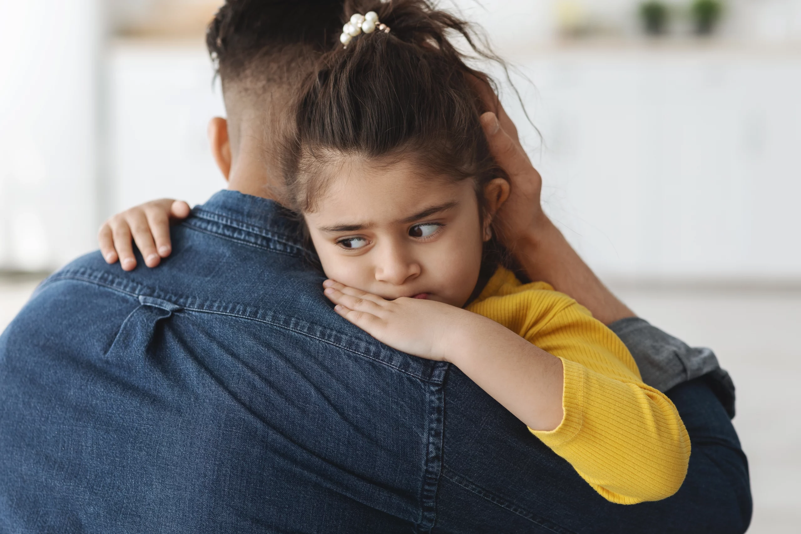 Young girl in yellow sweater hugging adult in denim shirt, looking worried, symbolizing emotional impact of unpaid child support in Washington